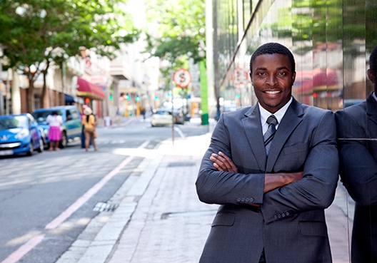A man standing in the street, with his arms crossed, smiling at the camera