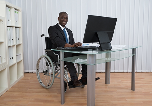 man sitting in a wheelchair behind his desk