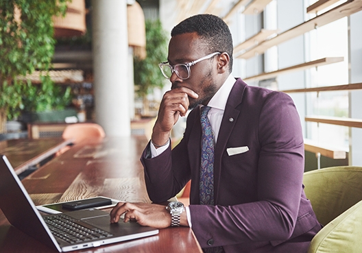 man sitting at a desk in an office foyer looking at his laptop