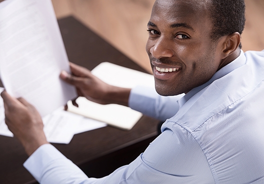 A financial adviser holds documents in his hands while sitting at his desk.