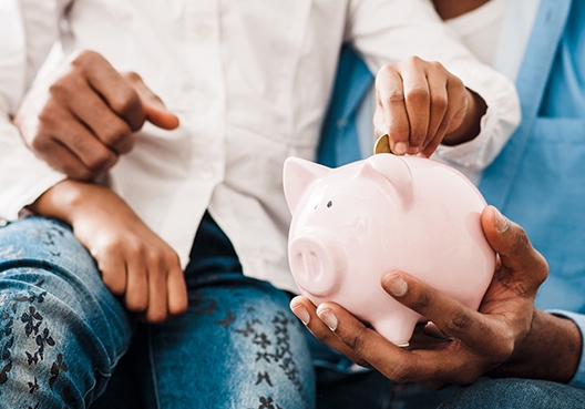 Elimika Education Plan father sitting with his daughter on his lap holding her piggy bank