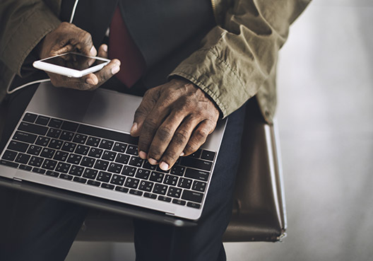 A male customer rests a hand on his laptop while holding his mobile phone in his other hand.