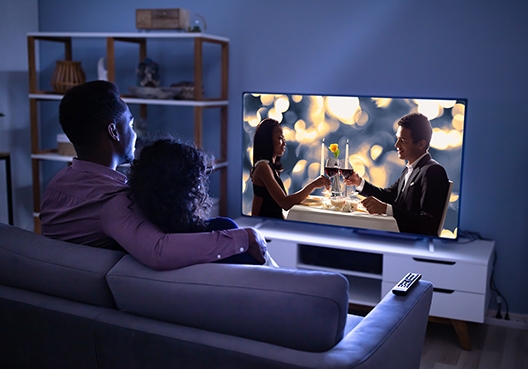 A couple sitting in the living room, at night, watching a movie